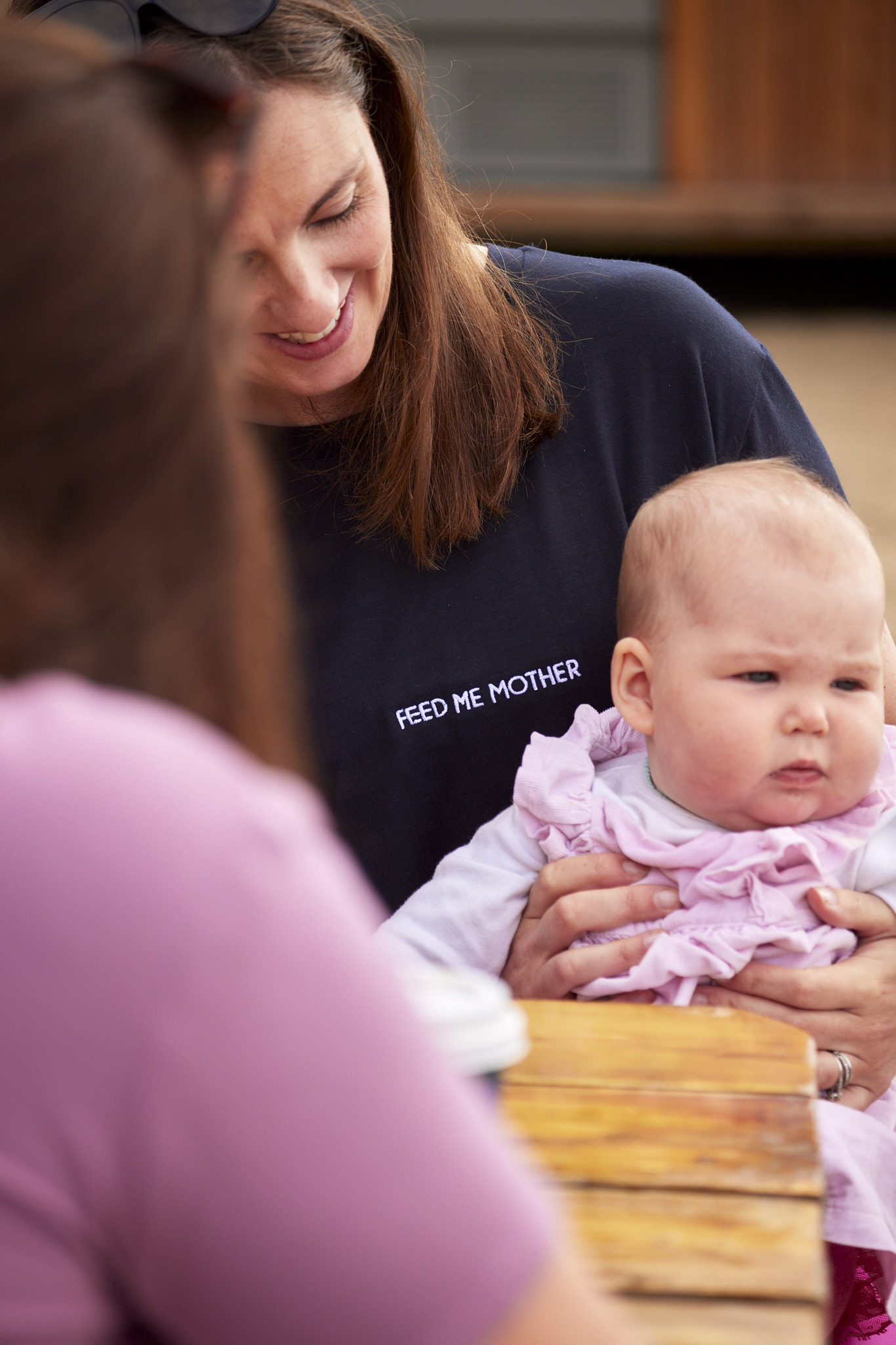 Woman wearing Feed Me Mother summer 2023 collection t-shirt while holding baby.