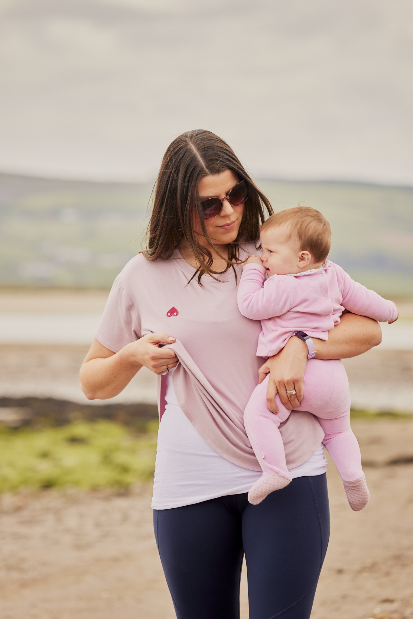 Woman playing on beach holding child wearing feed me mother apparel about to start breastfeeding.